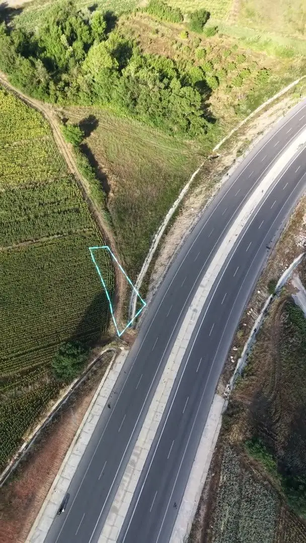 Gerçek drone karesi üzerine bindirilmiş neon parsel sınırı — karayolu kenarındaki tarlada cyan TKGM sınırı